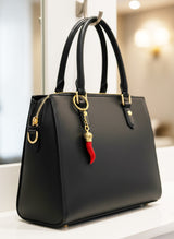 Black handbag with a red and gold charm on a blurred indoor background