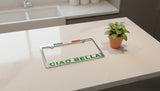 License plate frame with 'CIAO BELLA' text on a white surface next to a small potted plant.