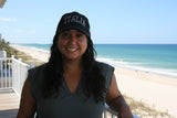 A woman wearing a black baseball cap featuring bold, all-caps “ITALIA” embroidery across the front in gray thread, standing on a beach. A brushstroke design in green, white, and red—representing the Italian flag—adorns the side, making this cap a stylish tribute to Italian pride and heritage.